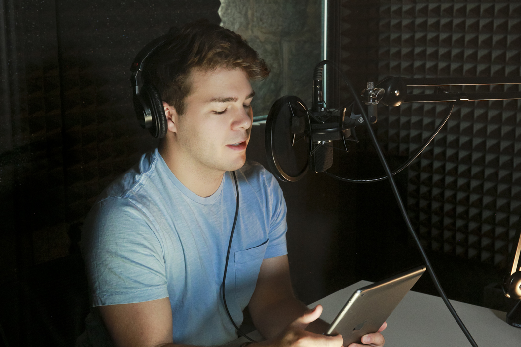 A man in an audio booth speaks into a microphone.